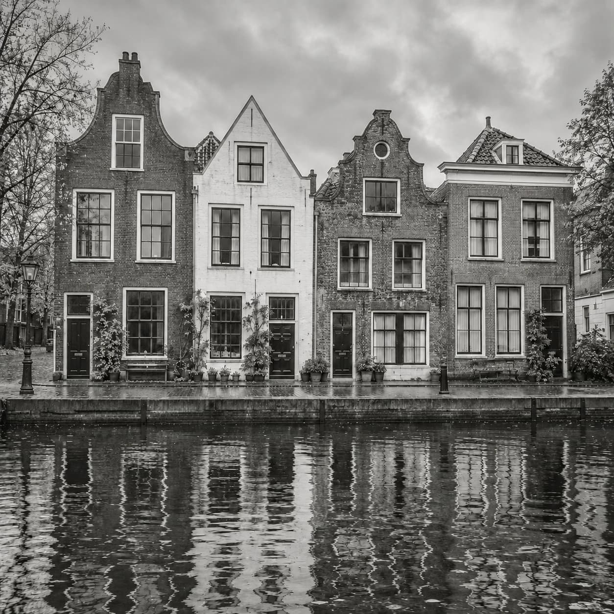 Artistiek zwart-witbeeld van vier verschillende Nederlandse grachtenhuizen die samen een gevelrij vormen, weerspiegeld in het water.